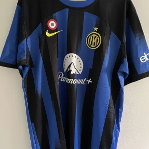 Inter Milan hemmatröja - Säljer en blå och svart randig Inter Milan fotbollströja från Nike med klubbmärke och sponsortryck på bröstet. Klassisk design med korta ärmar och rund hals. Perfekt för dig som älskar Serie A och vill visa ditt stöd för Inter.