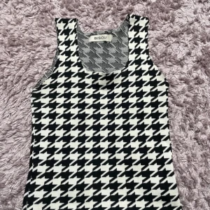 Svartvit croppad linnetopp från Bisou - Trendig croppad linnetopp från Bisou med svartvitt hundtandsmönster. Toppen är ärmlös och har rund halsringning. Perfekt att styla till både jeans och kjol för en cool look. Har inte alls använt för jag fick den i present och den är sprillans ny. 