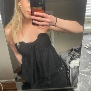 Svart tubtopp med knyt - Säljer en svart tubtopp med knyt framtill och broderade hål för en extra detalj. Toppen är ärmlös och har en luftig passform, perfekt för varma dagar eller sommarens alla tillfällen.💞💞