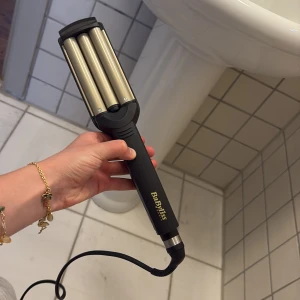 BaByliss vågtång med keramisk titanbeläggning - Säljer en BaByliss vågtång med keramisk titanbeläggning. Perfekt för att skapa snygga vågor i håret. Svart handtag med guldiga värmeplattor och justerbar temperatur. Utrustad med EU-kontakt. Använt en gång vid ett tilfälle. 