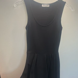 Svart ärmlös klänning från Pull&Bear baby doll  - En stilren svart ärmlös klänning från Pull&Bear med rund halsringning och utställd kjol. Perfekt för dig som gillar enkel och klassisk stil. Klänningen har en kort längd och är tillverkad i ett mjukt, följsamt material.