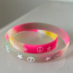 Färgglada armband med stjärnor och peace-symboler - Två coola armband i silikon med färgerna rosa, gul och grön. Båda har vita tryck med stjärnor och peace-symboler runt om. Perfekt accessoar för att liva upp din stil!