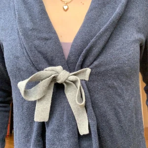 Mörkblå kofta med rosett från Odd Molly - Supersöt mörkblå kofta från Odd Molly med ljusgrå knytrosett framtill. Koftan har lång ärm, volangkant nedtill och broderad logga på ryggen. Perfekt för dig som gillar unika detaljer och mjuka material. Skulle säga att storlek 1 Odd Molly motsvarar ungefär xxs-xs eller ca 158 cm