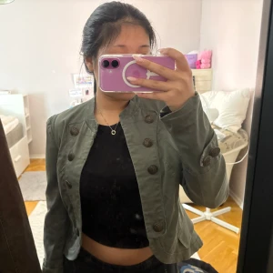 Mörkgrön jacka från Lindex - Snygg mörkgrön jacka från Lindex och dekorativa knappar framtill. Jackan är kortare i modellen och har långa ärmar samt rundad halsringning. Perfekt för att lyfta en enkel outfit.