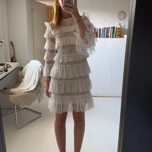 By malina klänning - Superfin vit kortklänning med volanger och spetsdetaljer. Klänningen har lång ärm och är genombruten med flera lager volanger. Perfekt för dig som vill sticka ut med en romantisk och trendig look. Halsen är nervikt på den första bilder. Klänningen är bara använd 1 gång, jätte bra skick! Kan tänka mig att gå ner i pris vid snabb affär 
