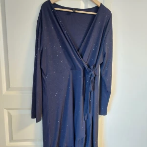 Mörkblå omlottklänning med glitter från SHEIN Curve - Säljer en mörkblå omlottklänning från SHEIN Curve i storlek 3XL. Klänningen har långa ärmar, knyt i midjan och är dekorerad med glittriga detaljer. Perfekt för dig som vill sticka ut lite extra!