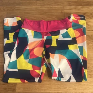 Färgglada träningstights från Adidas - Säljer ett par färgglada träningstights från Adidas med bred rosa midja och grafiskt mönster i blått, gult, orange, vitt och svart. Perfekta för dig som vill sticka ut på gymmet eller under löprundan!
