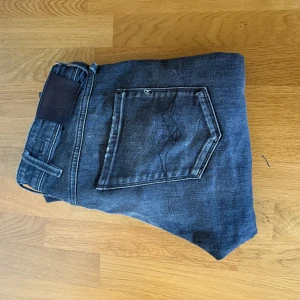 Mörkgrå jeansbyxor - Säljer ett par mörkgrå replay jeans med klassisk femficksdesign och normal passform. Byxorna har en lätt tvättad look och detaljer som bälteshällor och dragkedja. Perfekta för en avslappnad stil.