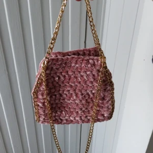 Rosa virkad väska med guldkedja - Superfin rosa väska med virkad struktur och snygga guldfärgade kedjor. Perfekt för att lyfta vilken outfit som helst med en söt och trendig touch. Väskan är mjuk och har en unik design som verkligen sticker ut.