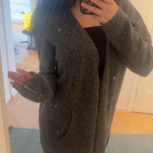 Mörkgrå lång kofta - Säljer en mysig och lång mörkgrå kofta med fickor framtill. Koftan har långa ärmar!