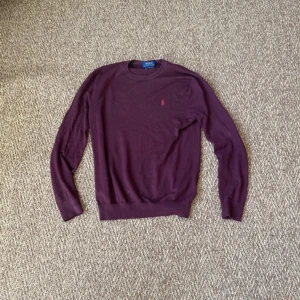 Vinröd merinoullströja från Polo Ralph Lauren - Vinröd långärmad tröja från Polo Ralph Lauren i tvättbar merinoull. Slim fit-modell med rund halsringning och diskret broderad logga på bröstet. Perfekt för dig som gillar klassisk och stilren design.