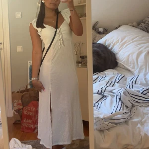 Vit långklänning med volang och knyt - Säljer en vit långklänning med volangdetaljer vid axlarna och knyt framtill. 