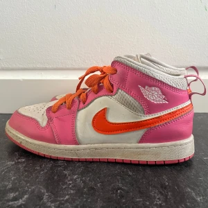 Jordan 1 Mid, Rosa & Orange - Strl 36 - Säljer ett par Jordan 1 Mid i vitt och rosa med orange swoosh och matchande snörning. Hög modell med klassisk Air Jordan-logga på sidan. Använda men i fint skick – lite smuts på sulan. Perfekta för dig som vill sticka ut!