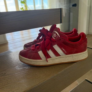 Röda Adidas Campus  - Säljer ett par röda Adidas Campus sneakers med vita ränder. Bra skick. Pris kan diskuteras vid snabb affär. Köpta för 1700. Bud tas emot! Hör av dig vid frågor! Köp gärna via ”köp nu”.
