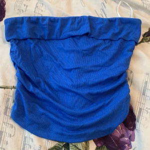 Blå ribbad tubtopp - Säljer en blå ribbad tubtopp med rynkade sidor och dragsko. Perfekt för dig som vill ha en enkel men snygg topp till sommaren. Toppens material är stretchigt och sitter bekvämt. Använd 1 gång är som ny men lite skrynklig 