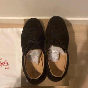 Svarta sneakers från Christian Louboutin - Säljer ett par svarta sneakers från Christian Louboutin med klassisk röd sula. Skorna har snörning och är tillverkade i skinn. Perfekta för dig som gillar stilrena och exklusiva sneakers. Kvitto finns även och självfallet äkta. Det är bra skick bara lite slitna på sulan 