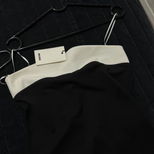 Svart och vit tub topp från Bik Bok - Säljer en svart tubklänning från Bik Bok med vit kant upptill. Klänningen har en enkel och stilren design utan axelband, perfekt för en trendig look.