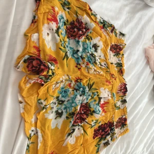 Gula blommiga shorts - Färgglada shorts i gult med stora blommiga mönster i vitt, blått och rött. De har en lös passform