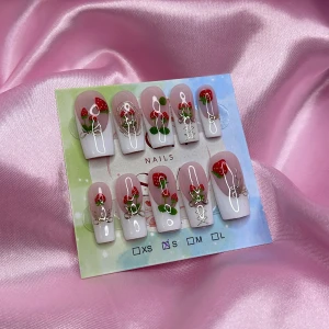 Strawbabe(S);Medium Square - Snygga gelè press on-naglar i storlek S: 15 mm, 11,5 mm, 12 mm, 11 mm, 9 mm , med ljusrosa bas, vita tippar och jordgubbsdekorationer. Naglarna har guldfärgade detaljer och små rosetter för extra effekt. Perfekt för dig som vill ha en söt och unik nagelstil utan att gå till salong.