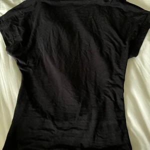 Svart topp med öppen rygg - Säljer en svart topp i mjuk bomull med korta ärmar och en riktigt snygg öppen rygg. Perfekt för dig som vill ha en basic men ändå unik look. Toppen har en tight passform och är enkel att matcha med både jeans och kjol.