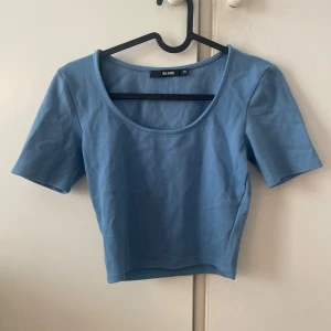 Blå croppad topp från Bik Bok - Säljer en ljusblå croppad topp från Bik Bok med korta ärmar och rundad, djup urringning. Toppen är i mjuk bomull och sitter tight mot kroppen, perfekt till jeans eller shorts för en chill look.