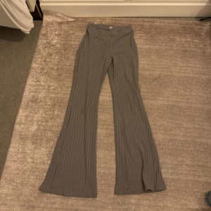 Grå ribbade bootcut byxor - Snygga grå ribbade byxor med bootcut-modell och hög midja. Byxorna har ett stretchigt material och raka, vida ben som ger en trendig siluett. Perfekta att styla med sneakers eller chunky boots.