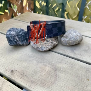 Svart rutigt bälte med silverdetalj - Snyggt svart bälte med rutigt mönster och silverfärgat spänne. Bältet har en stilren design och passar perfekt till jeans eller byxor för en cool look. Materialet är syntet och bältet har en klassisk form.