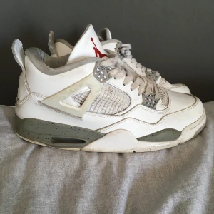 Nike Air Jordan 4 Retro Vit/Grå - Säljer ett par Nike Air Jordan 4 Retro i vitt och grått med röda detaljer. Skorna har klassisk meshpanel, snörning och den ikoniska Jumpman-loggan på plös och häl. Ovandelen är i skinn och mesh, sulan är gråspräcklig och har synlig Air-enhet.