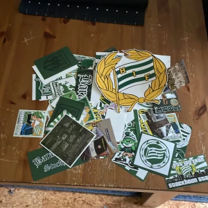 Ca 100st Hammarby klistermärken säljes som är i bra skick! - Bilden visar en samling klistermärken med Hammarby IF-tema, inklusive klubbens emblem och olika supporterrelaterade motiv. Ingen bok syns på bilden.
