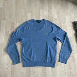 Blå tröja Polo Ralph Lauren - Snygg blå tröja från Polo Ralph Lauren i slim fit. Tröjan är tillverkad i mjuk pima bomull och har det klassiska broderade logotypen i gult på bröstet. Perfekt för dig som gillar stilrena och tidlösa plagg.