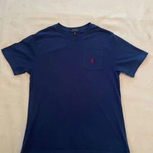 Blå t-shirt från Polo Ralph Lauren - Snygg blå t-shirt från Polo Ralph Lauren med v-ringning, storlek L för barn eller S för vuxna. Tveka inte med att skriva om ni har funderingar! 