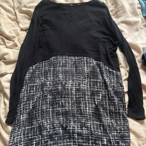 Svart och vit klänning från Isay - Snygg svart långärmad klänning från Isay med coolt rutigt mönster i vitt på nederdelen. Överdelen är helsvart och har en enkel, stilren design. Perfekt för dig som gillar en modern och avslappnad look.