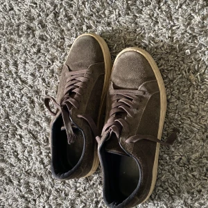Bruna mockasneakers från Vagabond - Snygga bruna sneakers från Vagabond i mocka med klassisk design och rund tå. Skorna har snörning och en beige platt sula som ger en clean look. Perfekta för dig som gillar stilrena och bekväma skor till vardags.