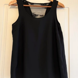 Svart linnetopp med spets från ONLY - Snygg svart linnetopp från ONLY i storlek 34. Toppen har en djup v-ringning i ryggen med transparent spetsdetalj som ger en extra touch. Ärmlös och i ett lätt, mjukt material som känns skönt mot huden. Perfekt att styla med jeans eller kjol.