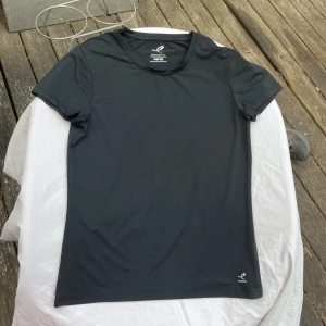 Svart sportig t-shirt från Energetics - En svart, stilren t-shirt från Energetics i ett mjukt och lätt material av 100% återvunnen polyester. Perfekt för träning med sin klassiska passform och korta ärmar. Diskret logga nertill och rund halsringning. Enkel och sportig vibe.