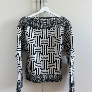 Svartvit stickad tröja med grafiskt mönster - Säljer en svartvit stickad tröja med ett riktigt coolt grafiskt mönster. Tröjan har långärmade ärmar och bred ribbstickad kant vid hals, ärmslut och nederkant. Perfekt för dig som gillar unika och iögonfallande plagg!