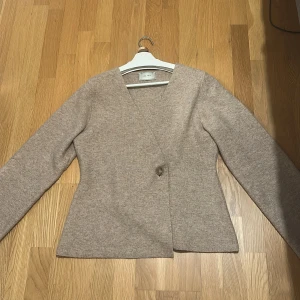 Beige stickad kofta från Neo Noir  - Snygg och felfri stickad kofta med djup hals. Säljer eftersom den inte kommer till användning längre och eftersom jag köpte den för ett högt pris tänkte jag sälja den. Den är i storlek 38 men den skulle absolut fungera för någon i storlek 36 med. 