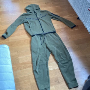 Grön Nike Tech - Säljer min gröna Nike tech då jag växt ur den, helt okej skick liten defekt på vänstra armen men inget som syns, och Nike logan på byxorna missfärgat sig lite men annars är den riktigt skön att ha på sig, om du vill köpa bara byxan elr koftan skriv i dm 