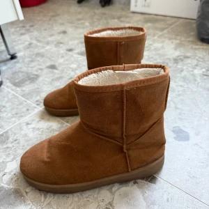 Bruna fodrade boots i mocka-look - Mysiga bruna boots med mjukt foder och mocka-liknande utsida. Skorna har platt sula med bra grepp och rund tå. Perfekta för kalla dagar när du vill hålla fötterna varma och sköna.