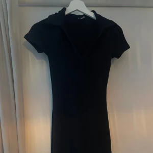 Svart ribbad kortklänning med krage - Svart ribbad kortklänning från H&M med v-ringning och krage. Klänningen har korta ärmar och en figurnära passform. Använd fåtal gånger, stretchiga material, skulle säga att den passar både S och M.