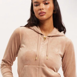 Beige velour hoodie från Juicy Couture - Supermjuk beige hoodie från Juicy Couture i velour med guldfärgade detaljer på snörningen och dragkedja. Klassisk broderad JC-logga på bröstet, huva och känguruficka framtill. Perfekt för en chill och trendig look. Lappen sitter kvar.  Kan tänka mig sänka priset💕