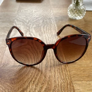 Bruna leopardmönstrade solglasögon H&M - Snygga solglasögon från H&M med rundad form och leopardmönstrad båge i bruna och svarta toner. Glasen är lätt tonade och ger en cool vintagekänsla. Perfekta för att lyfta din stil under soliga dagar.