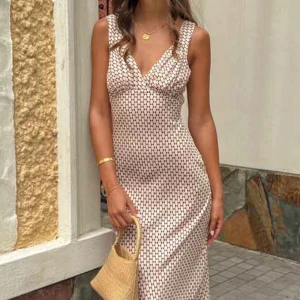 Beige mönstrad långklänning - Supersnygg långklänning i beige med brunt  mönster. Djup v-ringning, ärmlös och med knytband i ryggen för extra passform. Klänningen har en figurnära siluett och är perfekt för sommaren! 