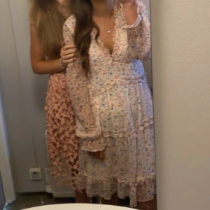 Blommig kortklänning från Vero Moda - Supersöt kortklänning från Vero Moda i ljus bas med små blommor i rosa, blått och grönt. Klänningen har v-ringning, volangdetaljer och långa ärmar med resår vid handlederna. Perfekt för sommarens alla tillfällen!