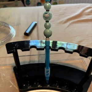 Stift penna  - Bilderna visar en blå penna dekorerad med pärlor, inklusive en med en söt hundfigur. Pennan står i ett svart ställ. 