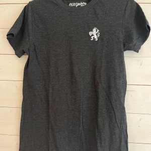 Mörkgrå IFK Göteborg t-shirt S - Mörkgrå t-shirt från IFK Göteborg Premium Edition med vit broderad klubb-logga på bröstet. Klassisk rund hals och korta ärmar. Skön och enkel stil som passar perfekt för dig som vill visa ditt lagstöd på ett snyggt sätt.
