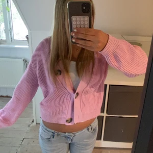 Rosa stickad kofta från H&M - Superfin ljusrosa stickad kofta från H&M med stora knappar framtill. Koftan är croppad, har lång ärm och en relaxed fit. Perfekt att slänga över ett linne eller t-shirt för en chill look. Ribbstickad struktur som ger en trendig vibe.