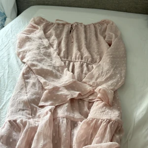 Ljusrosa prickig klänning H&M Divided - Supersöt ljusrosa klänning från H&M Divided i storlek 36. Klänningen har långärmade ärmar, volangdetaljer och ett diskret prickigt mönster. Den är tillverkad i ett lätt och luftigt tyg, perfekt för vår och sommar. Snygg offshoulder-modell med knyt i halsen.