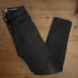 Jacob Cohën grå Nick Slim jeans - Snygga grå jeans från Jacob Cohën i modellen Nick Slim. Jeansen har fem fickor och klassiska sömmar. De är tillverkade i mjukt denimtyg och har en slim passform med normal midja. Perfekta för dig som gillar stilrena och bekväma jeans. Nästan oanvänd och det förekommer inga defekter. Tveka inte att höra av er och kan tänka mig sänka priset vid snabb affär!