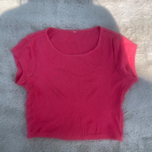 Ribbad rosa croppad topp - En söt croppad topp i stark rosa färg med ribbad struktur. Modellen är ärmlös med rund halsringning och har en tight passform som sitter snyggt. Perfekt för varma dagar eller när du vill ha en enkel men trendig look.